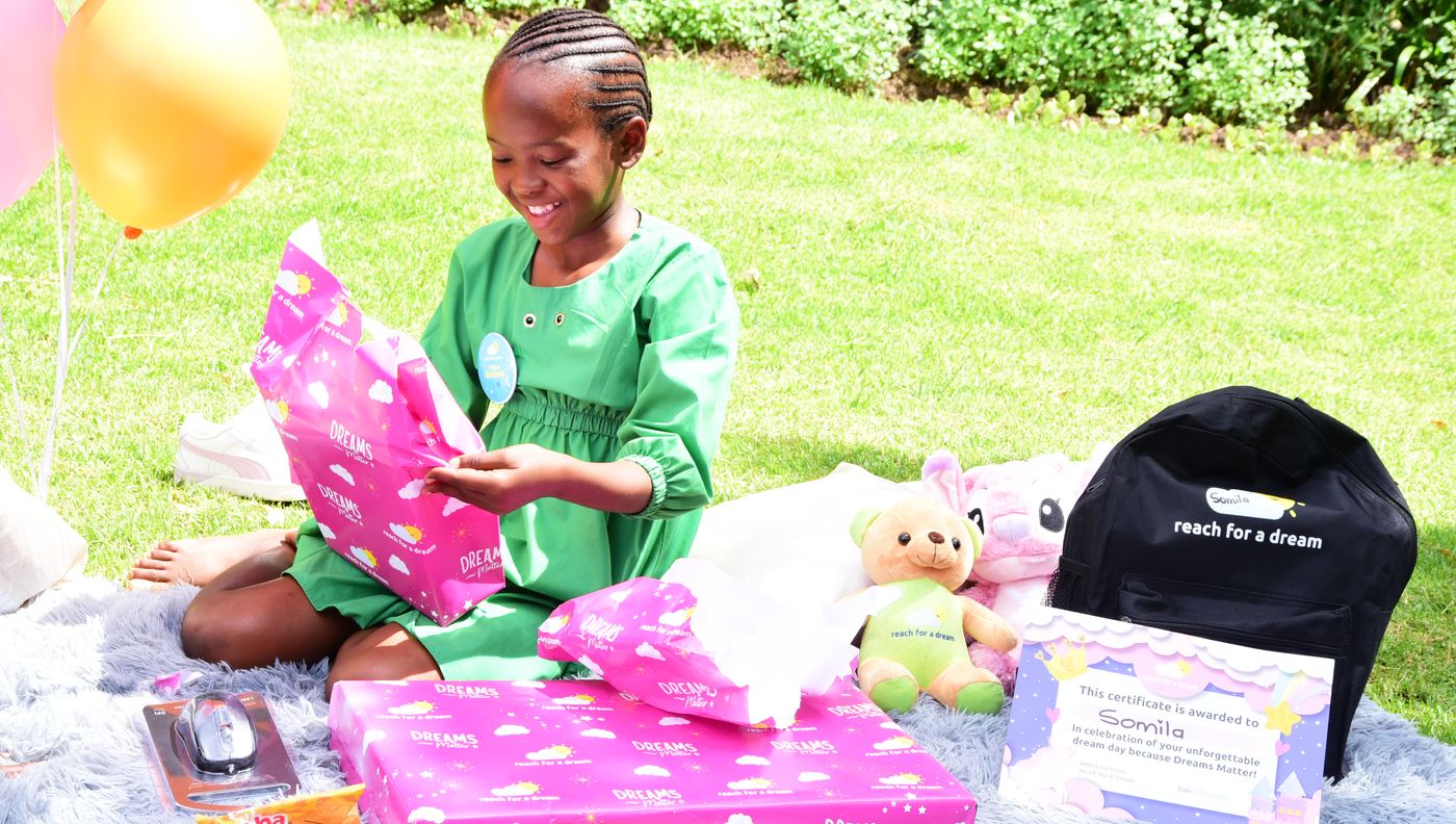 A girl in a green dress unwrapping gifts on a blanket in a sunlit garden